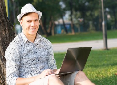 Parkta dizüstü bilgisayarla çalışan genç bir adam.