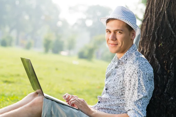 Jovem trabalhando no parque com um laptop — Fotografia de Stock