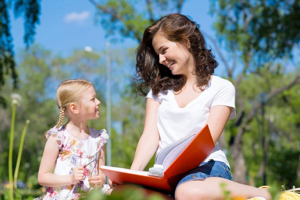 Flicka och en ung kvinna läser en bok tillsammans — Stockfoto