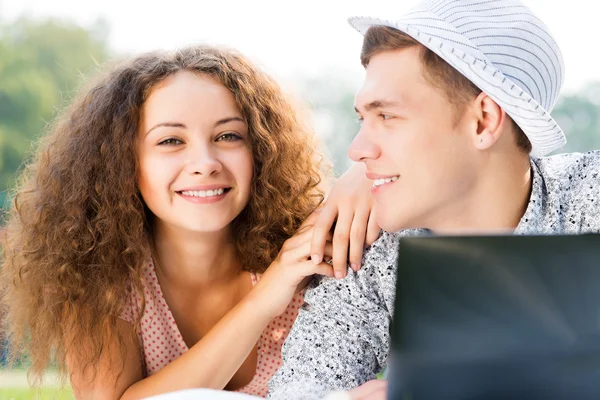 Couple lying together in a park with laptop — Stock Photo, Image