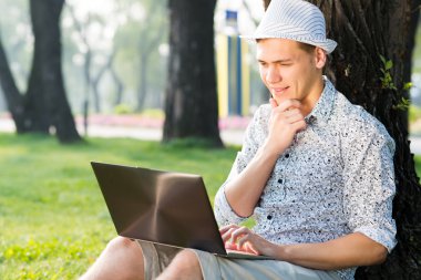 Parkta dizüstü bilgisayarla çalışan genç bir adam.