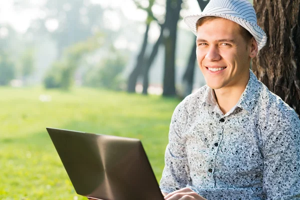 公園でノートパソコンを持って働いている若い男が — ストック写真