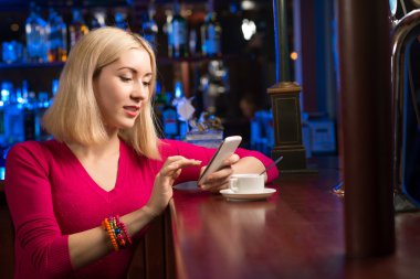 bir fincan kahve ve cep telefonu olan kadın