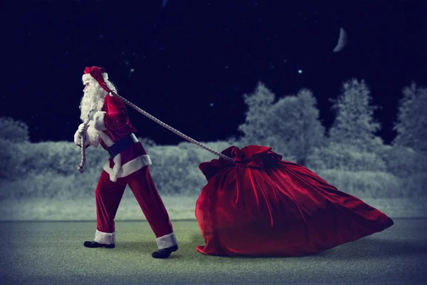 Санта Клаус вытаскивает огромный мешок с подарками — стоковое фото