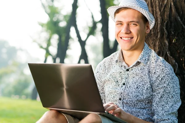 Mladý muž pracující v parku s laptopem — Stock fotografie