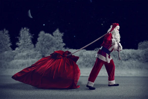 Санта Клаус вытаскивает огромный мешок с подарками — стоковое фото