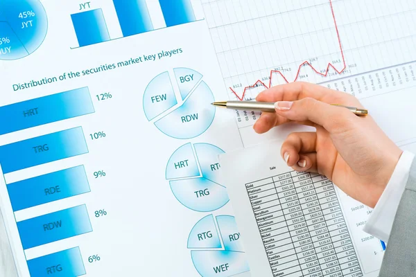 Female hand pointing pen on financial charts — Stock Photo, Image
