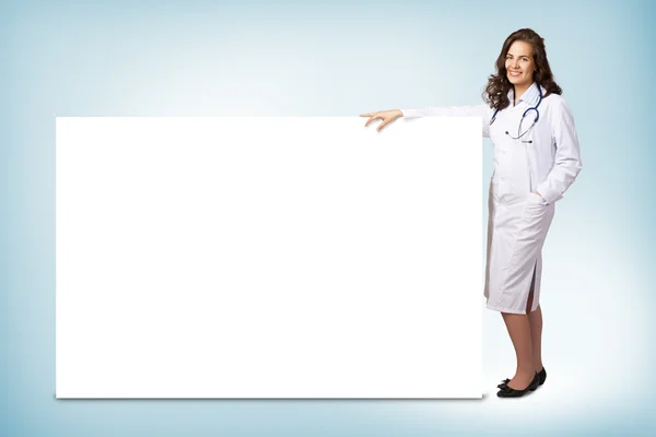 Young woman doctor standing near a blank banner — Stock Photo, Image