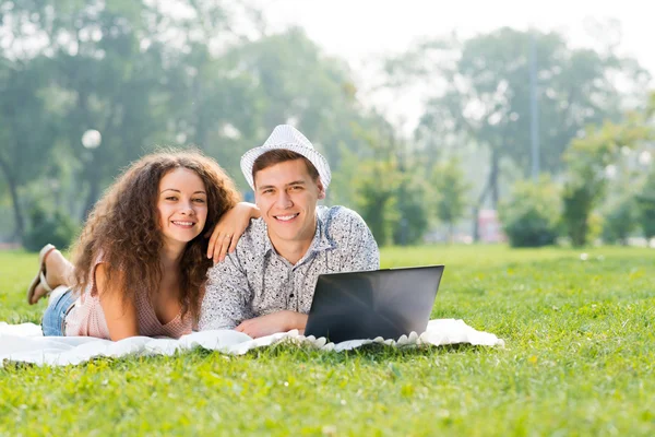 Par liggande tillsammans i en park med laptop — Stockfoto