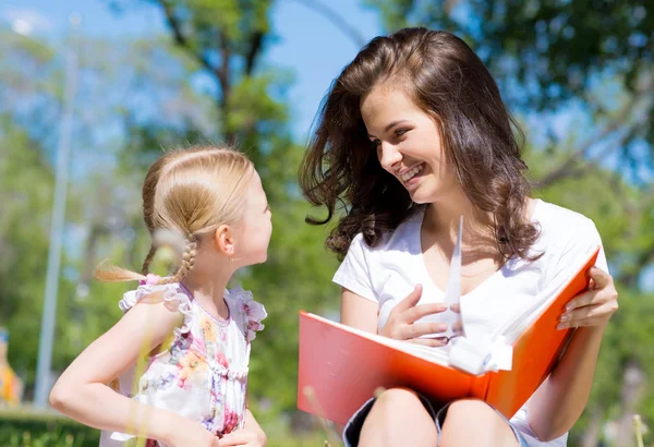 Menina e uma jovem mulher lendo um livro juntos — Fotografia de Stock