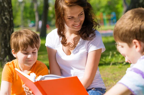 Enseignant lit un livre aux enfants dans un parc d'été — Photo