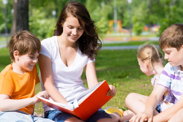 Enseignant lit un livre aux enfants dans un parc d'été — Photo