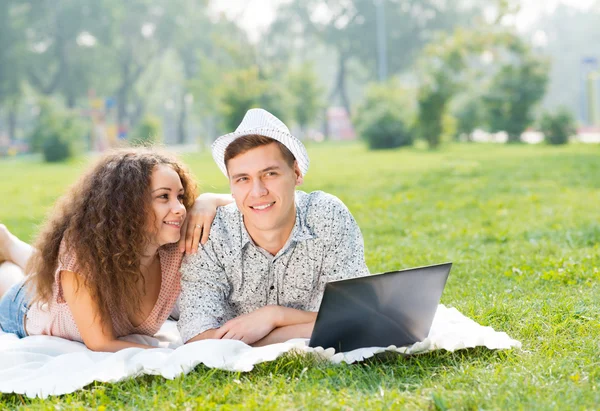 Par liggande tillsammans i en park med laptop — Stockfoto