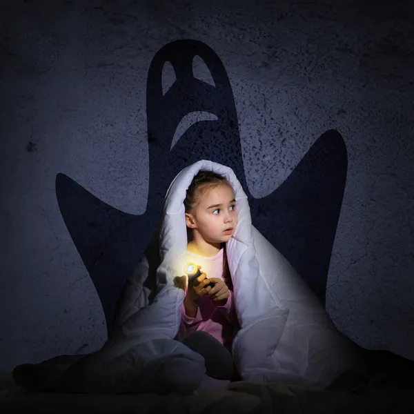 Flicka under täcket med en ficklampa — Stockfoto