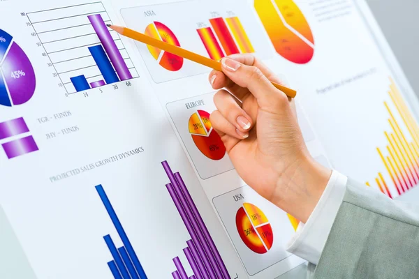 Female hand pointing pencil on financial charts — Stock Photo, Image