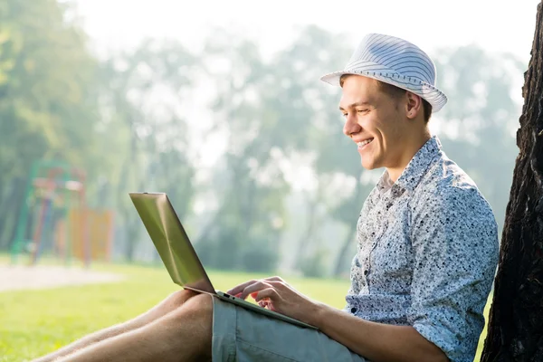 Jovem trabalhando no parque com um laptop — Fotografia de Stock