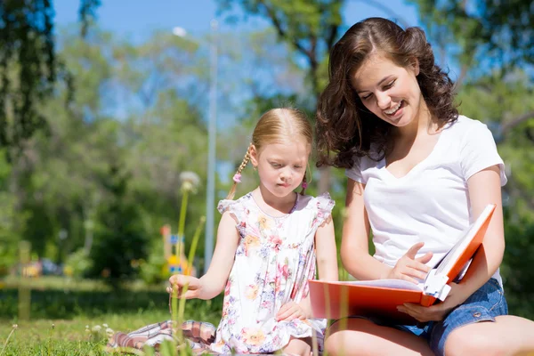 Menina e uma jovem mulher lendo um livro juntos — Fotografia de Stock