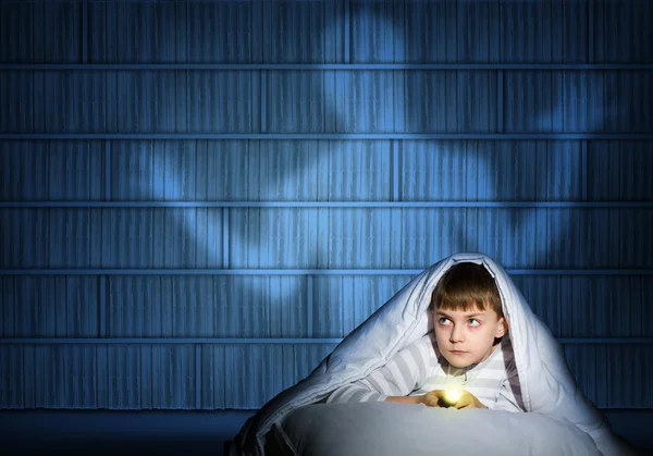 Ragazzo sotto le coperte con una torcia elettrica — Foto Stock