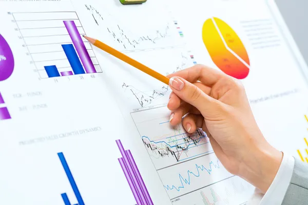 Female hand pointing pencil on financial charts — Stock Photo, Image