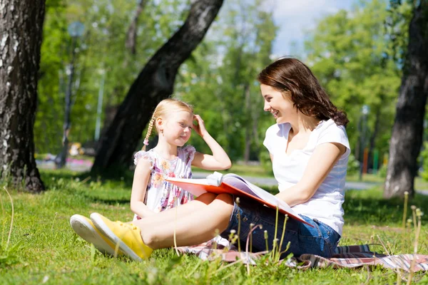 Flicka och en ung kvinna läser en bok tillsammans — Stockfoto