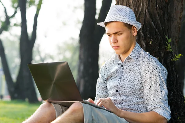 Jovem trabalhando no parque com um laptop — Fotografia de Stock