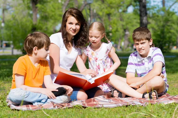 Professor lê um livro para crianças em um parque de verão — Fotografia de Stock
