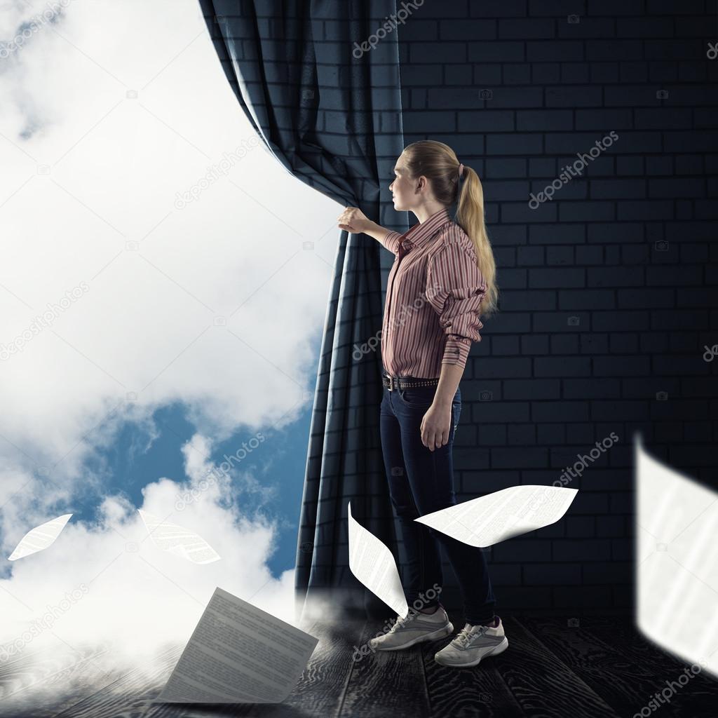 young woman pushes the curtain looking at clouds