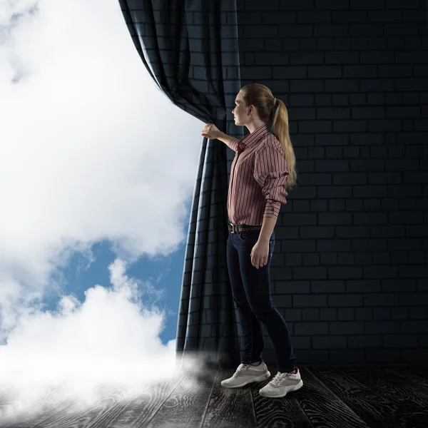 Junge Frau schiebt den Vorhang und blickt auf Wolken — Stockfoto