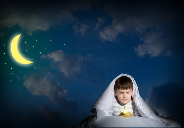 Pojke under täcket med en ficklampa — Stockfoto