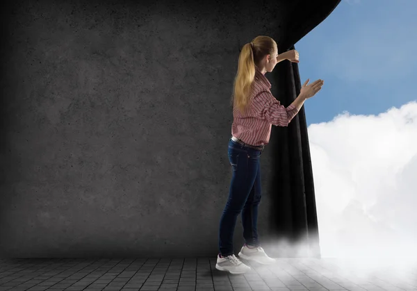 Jonge vrouw duwt het gordijn kijken naar wolken — Stockfoto