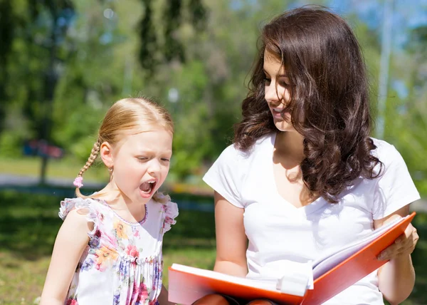 Menina e uma jovem mulher lendo um livro juntos — Fotografia de Stock