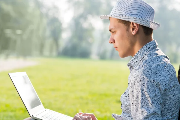 Giovane che lavora nel parco con un computer portatile — Foto Stock