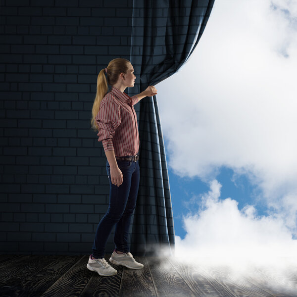 Молодая женщина поднимает занавес, глядя на облака.
