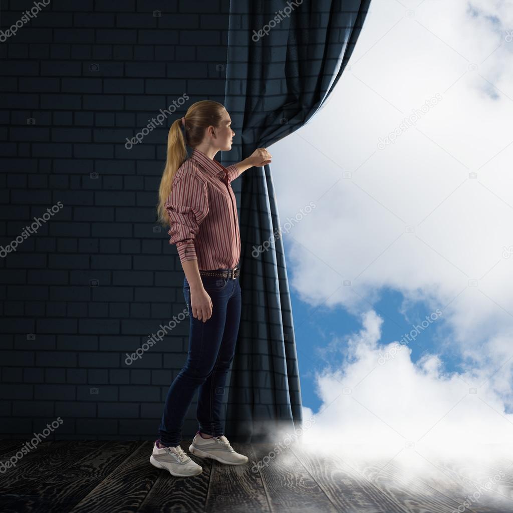 young woman pushes the curtain looking at clouds