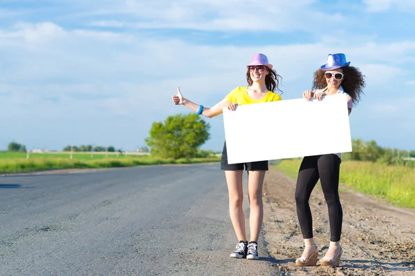 Two young women stand with a blank banner — Stock Photo, Image