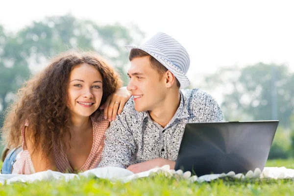 Par liggande tillsammans i en park med laptop — Stockfoto