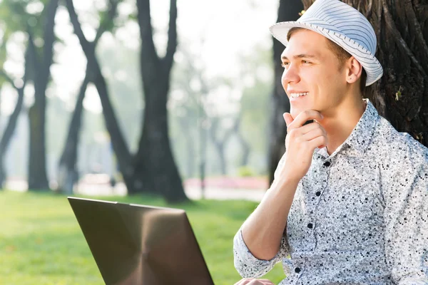Mladý muž pracující v parku s laptopem — Stock fotografie