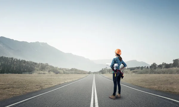 Jovem mulher em capacete de segurança em pé na estrada — Fotografia de Stock