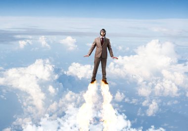 Takım elbiseli ve havacı şapkalı bir iş adamı gökyüzünde uçuyor.