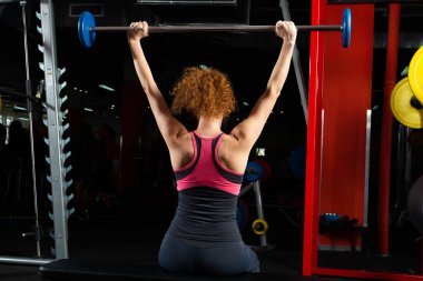 Vücut geliştiren kadın, spor salonunda halterle bağlanmış.