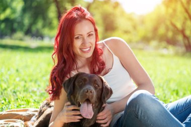 Genç ve çekici bir kadın parkta köpeğine sarılıyor..