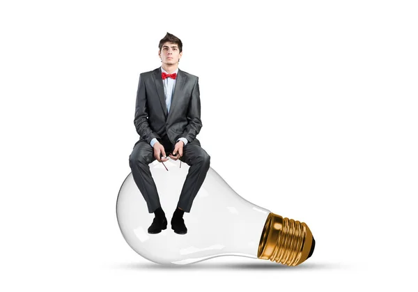 Young businessman sits on a light bulb — Stock Photo, Image