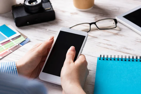 Blogger sentado en el escritorio y sosteniendo el teléfono inteligente —  Fotos de Stock