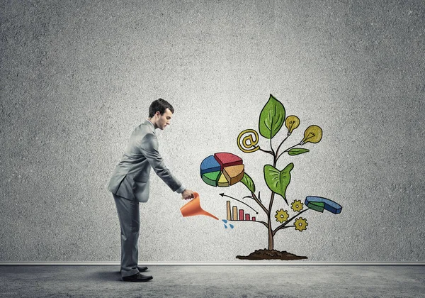 Young businessman in empty room watering drawn growth concept wi — Stock Photo, Image