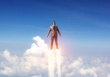 Takım elbiseli ve havacı şapkalı bir iş adamı gökyüzünde uçuyor.