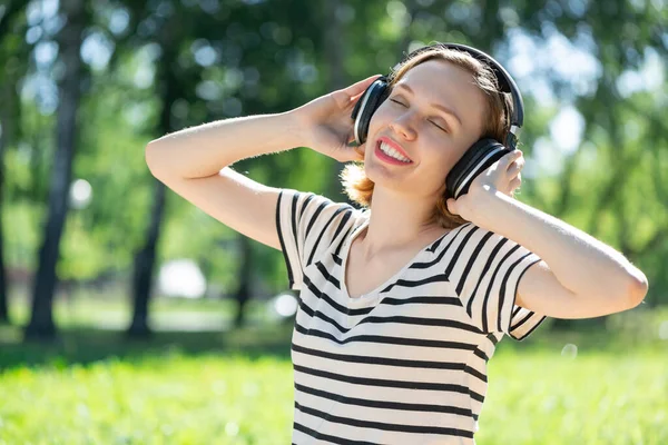Młoda kobieta ma muzykę w letnim parku. — Zdjęcie stockowe