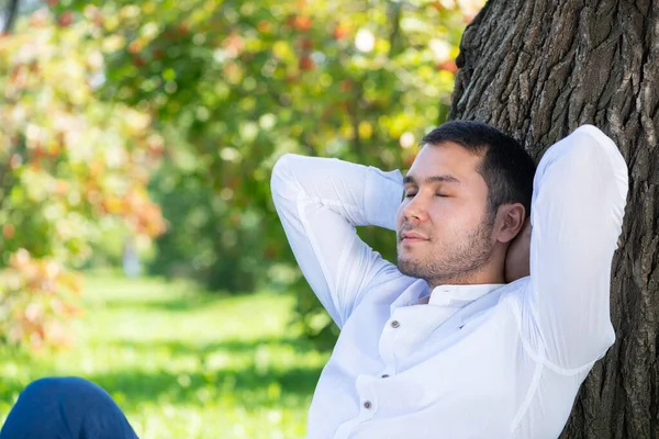 Joven sentado bajo el árbol en el parque en un día soleado — Foto de Stock