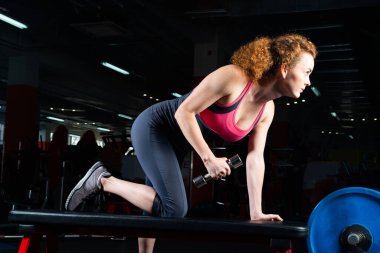 Spor salonunda dambıllarla nişanlı çekici genç bir kadın..