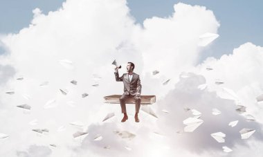 Hoparlörden bir şey anons eden bir iş adamı ve kağıt uçaklar etrafta uçuyor.