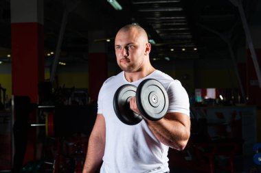 Spor salonunda dambıllarla çarpışan erkek vücut geliştirici.